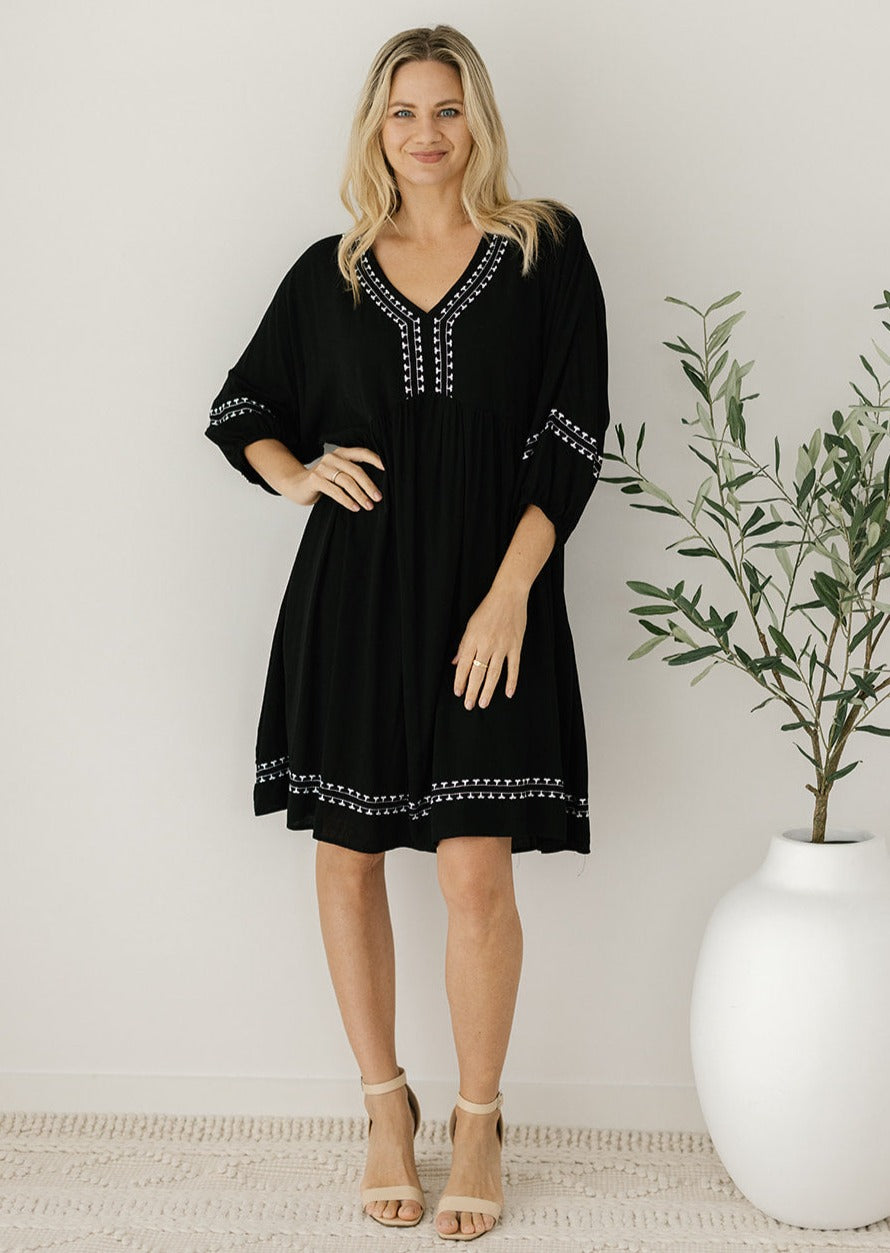 black knee-length dress with white embroidery detail